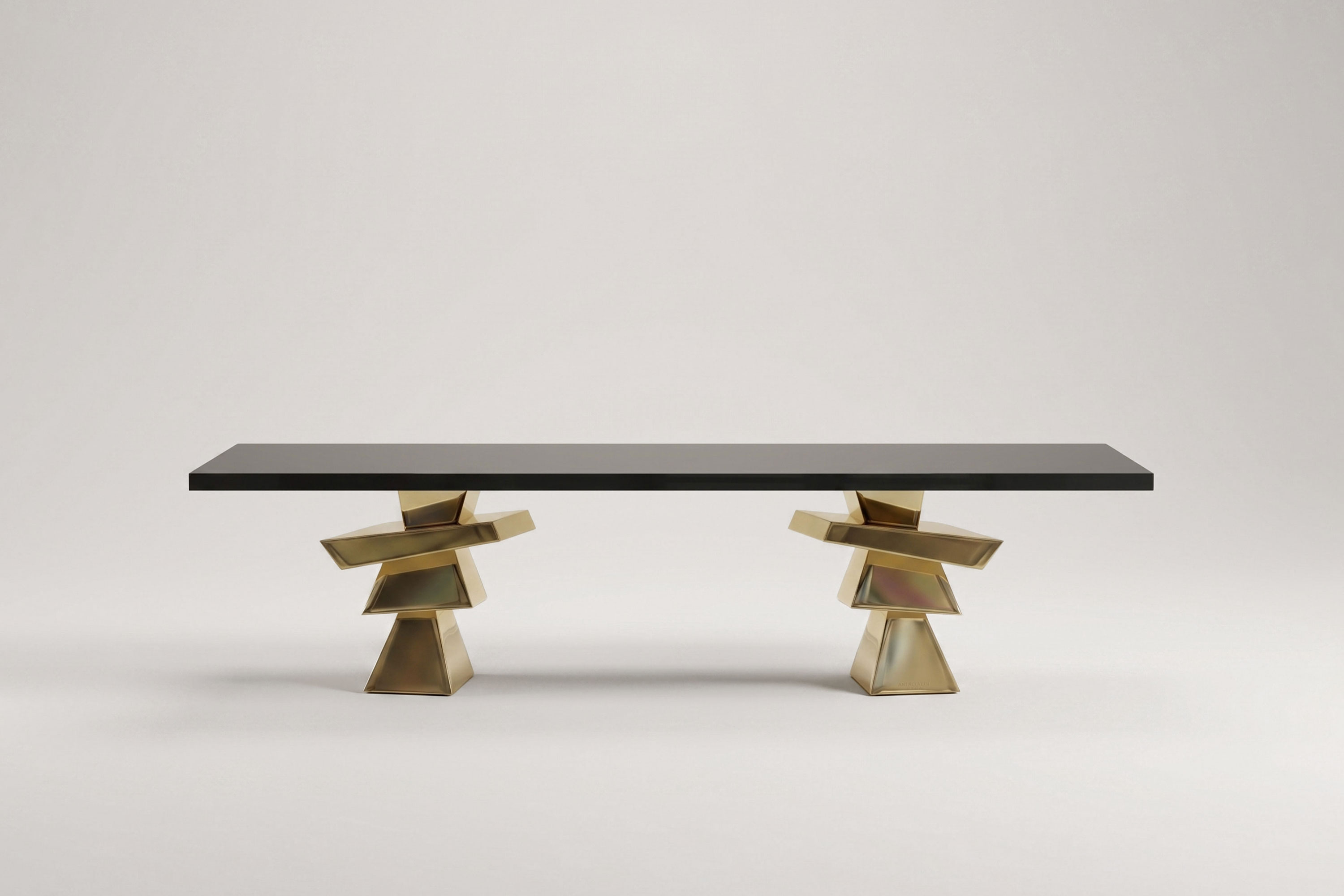 A modern rectangular table with a black top and two geometric, metallic gold bases featuring stacked angular shapes, set against a plain light background. This bespoke furniture piece draws inspiration from Artdecoo design.
