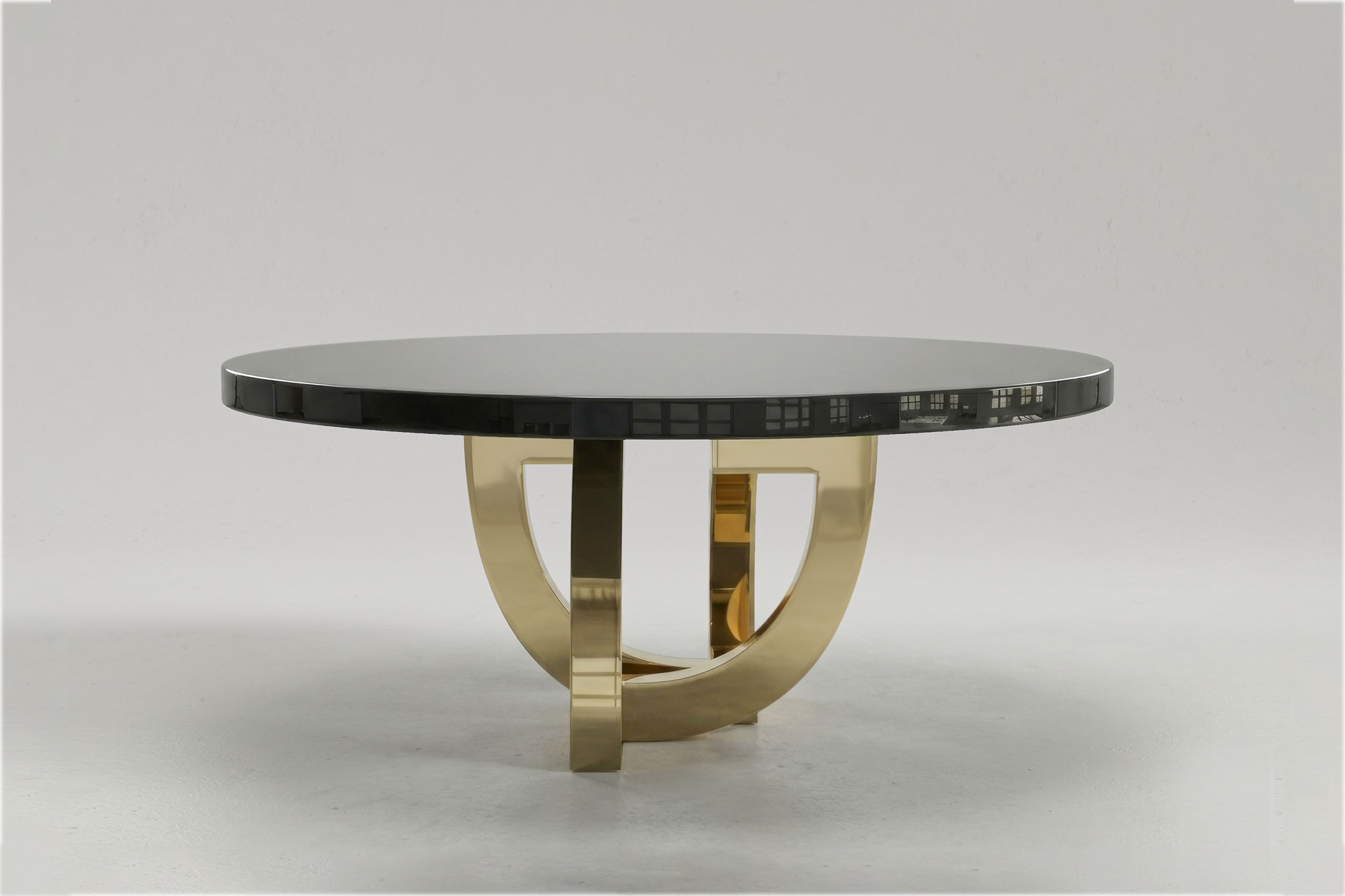 Arco Round dining table by Palena Studio, side view showing the curved arches of the polished bronze base beneath the round obsidian lacquer top