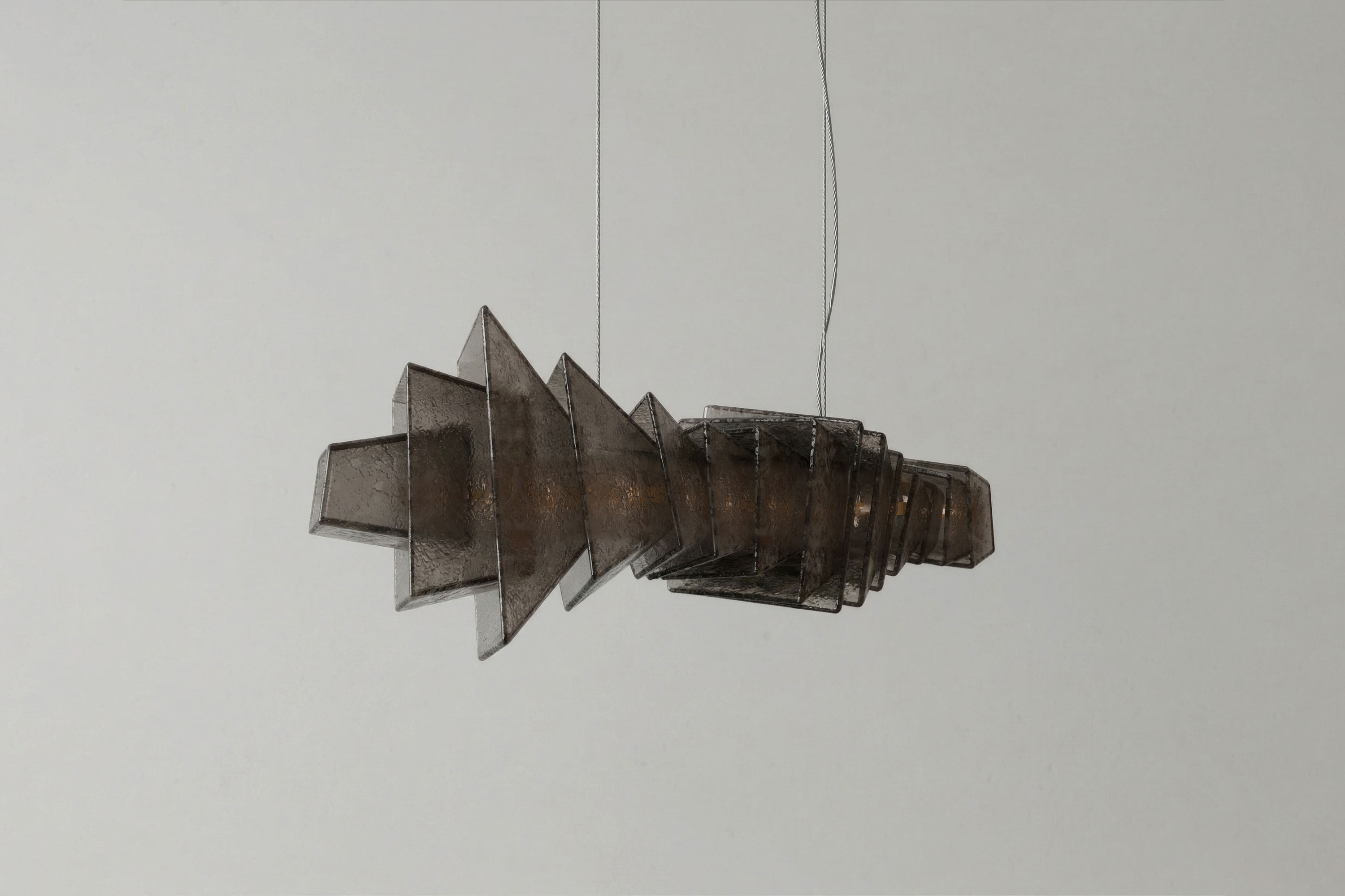 A modern pendant light with a geometric, layered design made of translucent, smoky Murano glass hangs from two thin cords against a plain, light-colored wall.