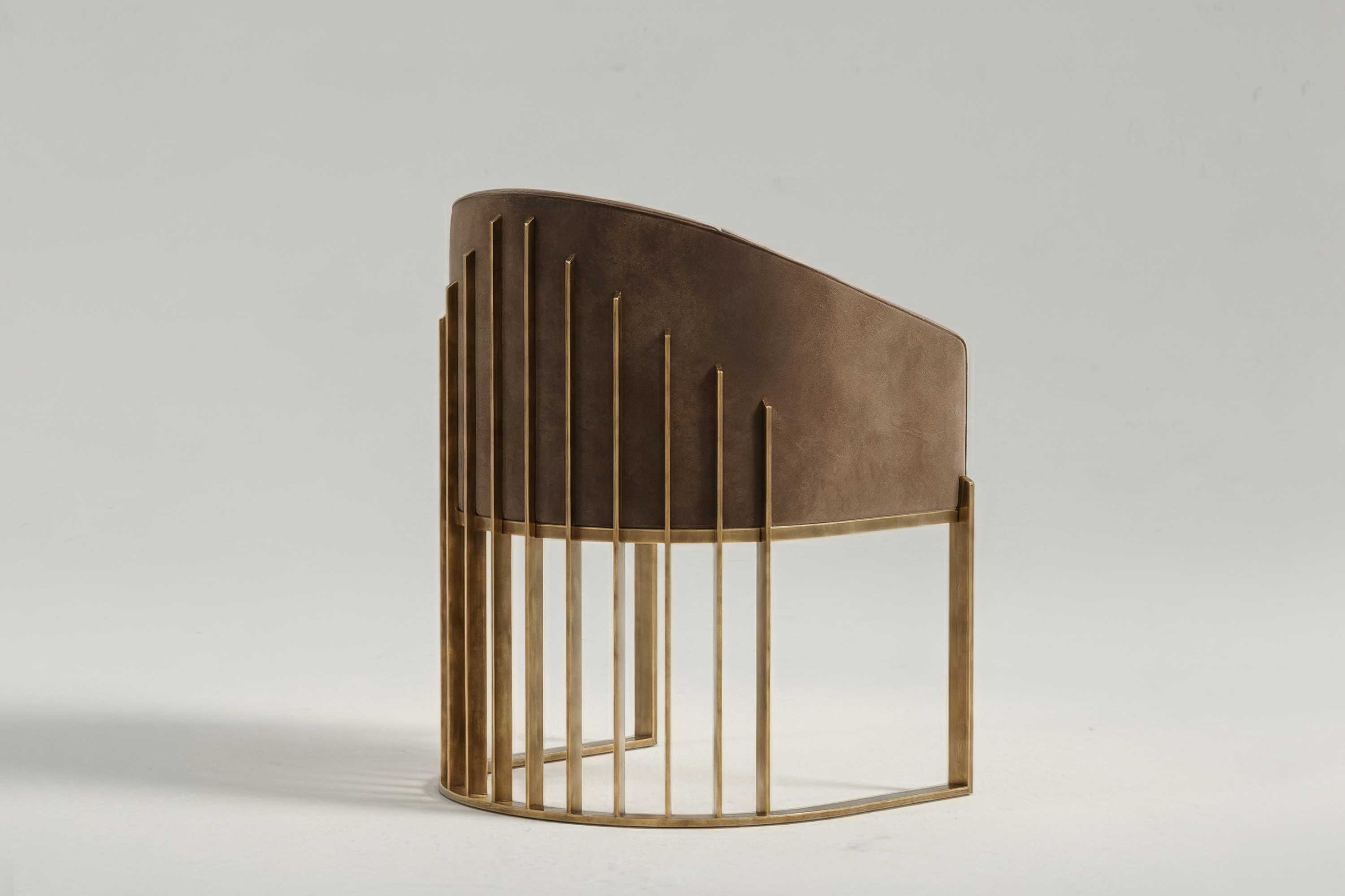 A modern chair with a brown upholstered curved backrest and thin, vertical bronze metal bars forming the base and sides, set against a plain light background.