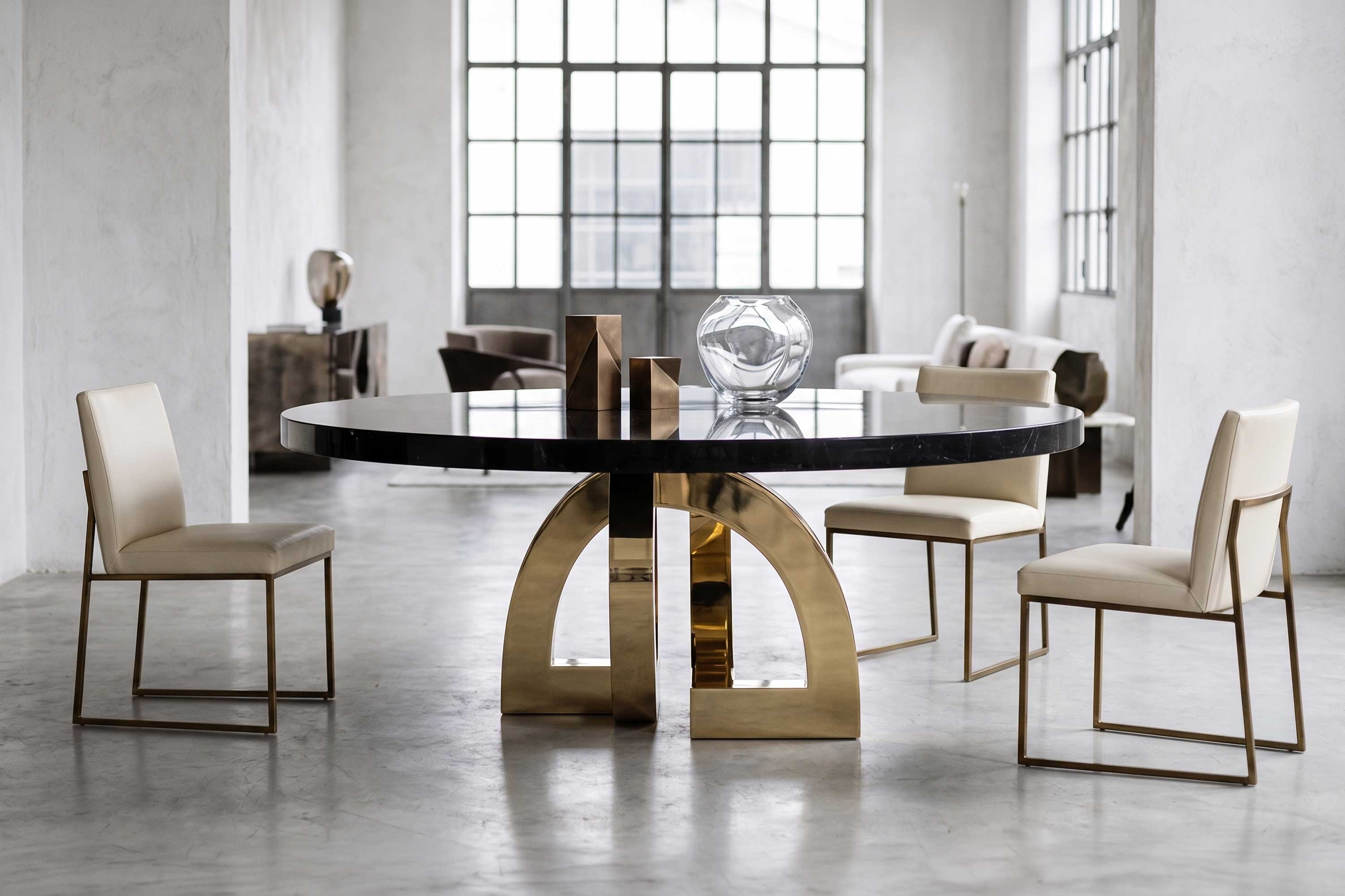 Arco Dining Table in polished bronze, sculptural arc-base dining table staged in a refined loft interior with industrial windows, Palena Studio