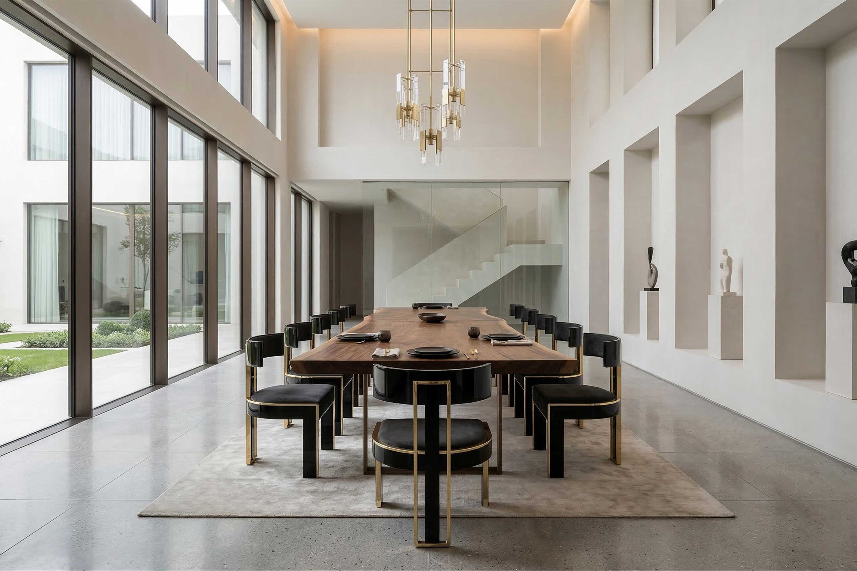 Modern dining room with a long wooden table, twelve black chairs with gold accents, large windows, sculpture niches on the right wall, and glass staircase in the background. Minimalist decor and neutral color palette throughout.