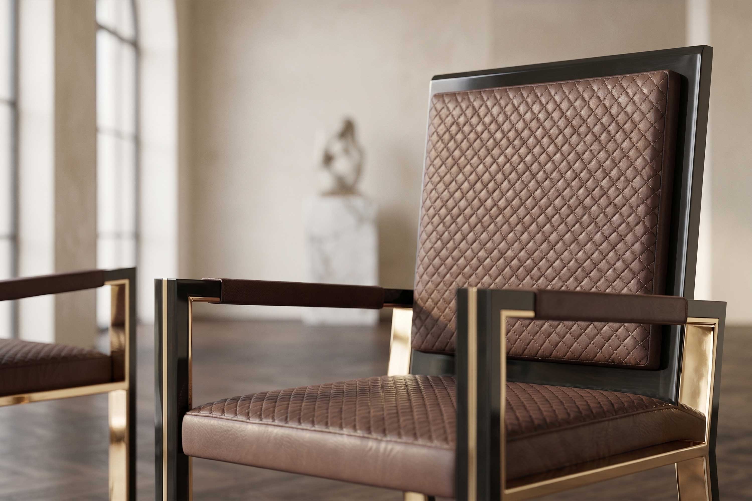 A modern chair with a quilted brown leather seat and backrest, featuring gold metal armrests and frame, sits in a spacious room with wooden floors and a blurred sculpture in the background.