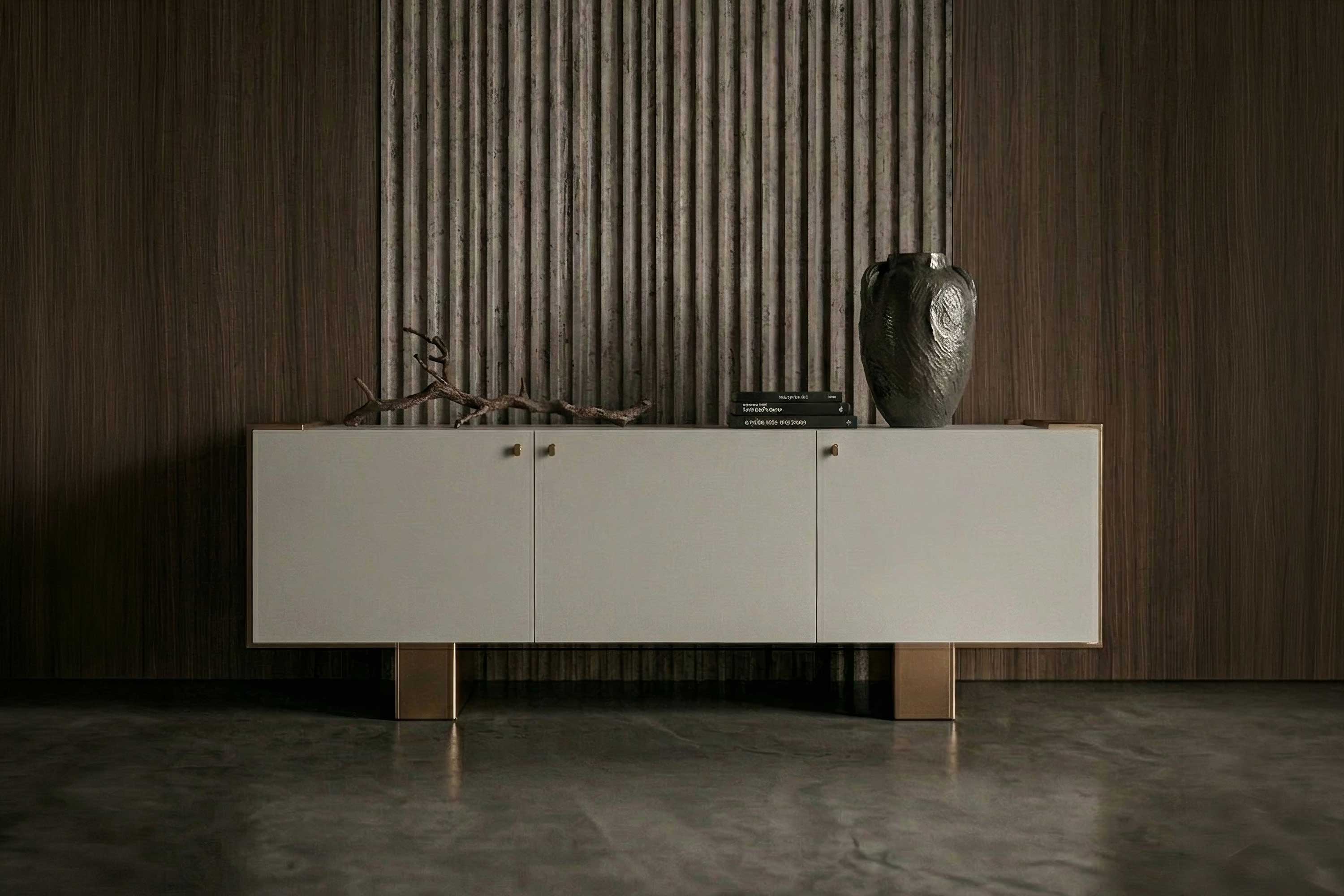 A modern sideboard with white cabinet doors and wooden legs stands against a brown wood-paneled wall. A metallic vase, two books, and a decorative branch are on top. The floor is polished concrete.