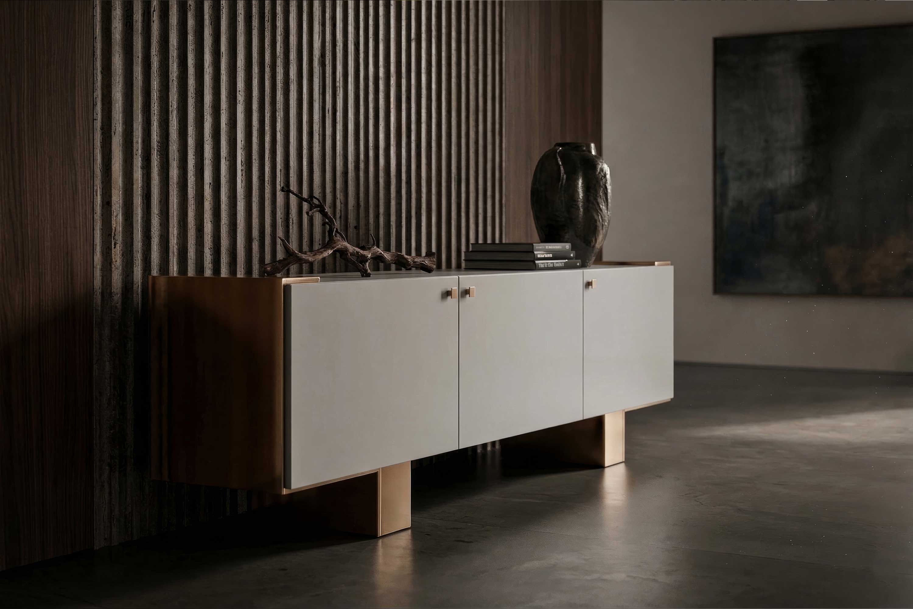 A modern sideboard with four doors stands against a textured wall. The sideboard has a light front, wooden top and legs, and is decorated with a black vase, stacked books, and a branch. The lighting is soft and minimal.