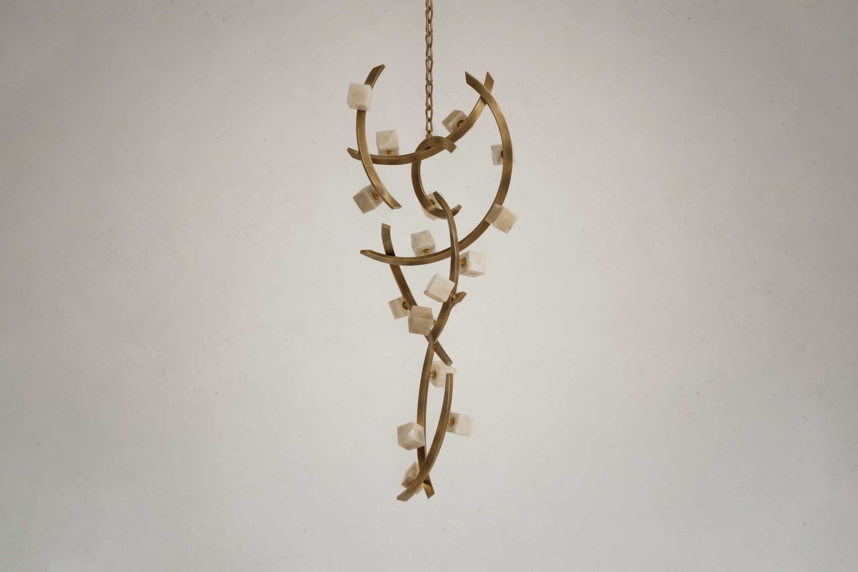 A sculptural Artdecoo chandelier with curved bronze arms and small white cube-shaped lights is suspended from a chain against a plain off-white wall background.
