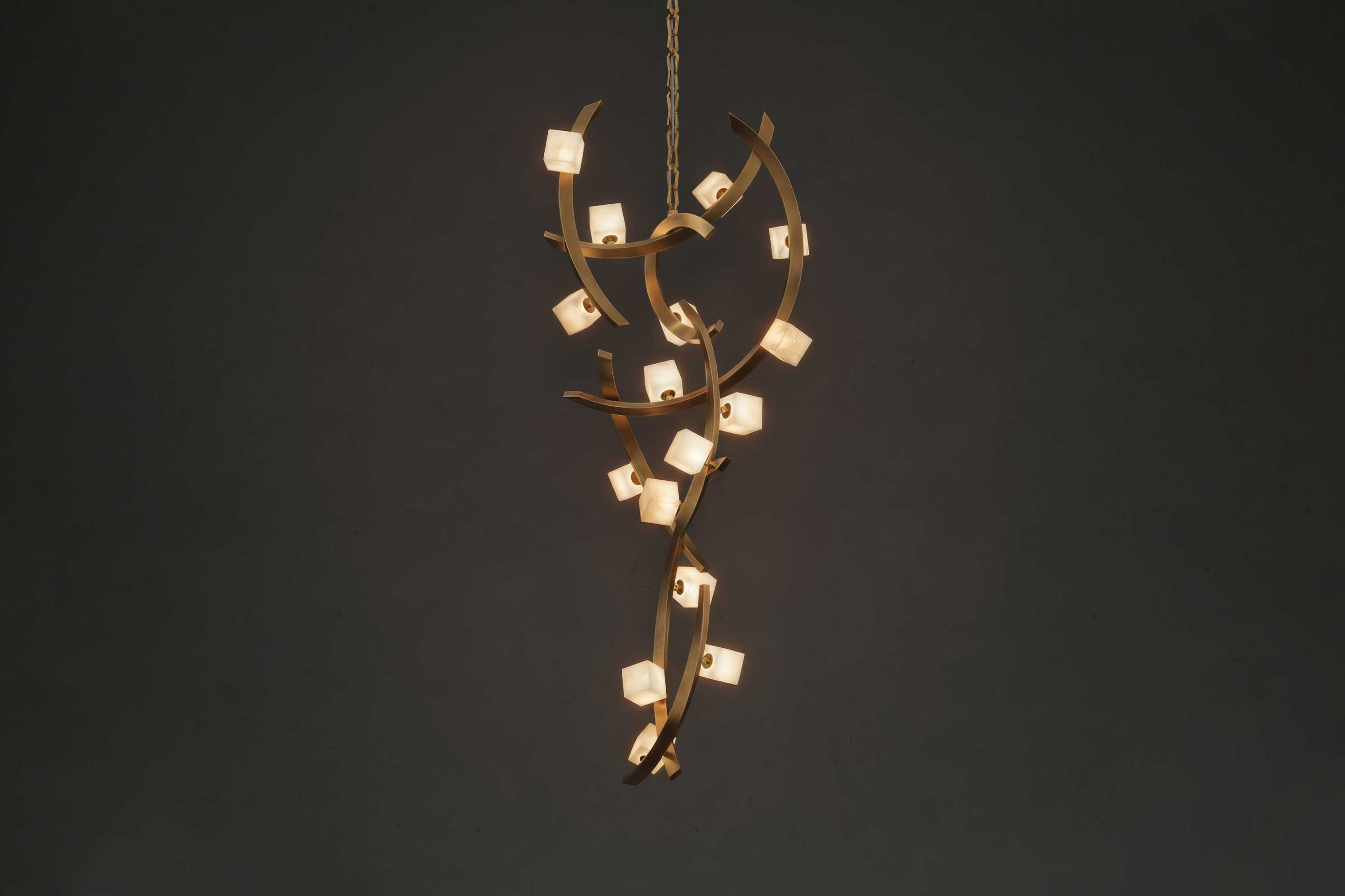 A modern chandelier with twisting bronze branches and small square lights, hanging against a dark background.