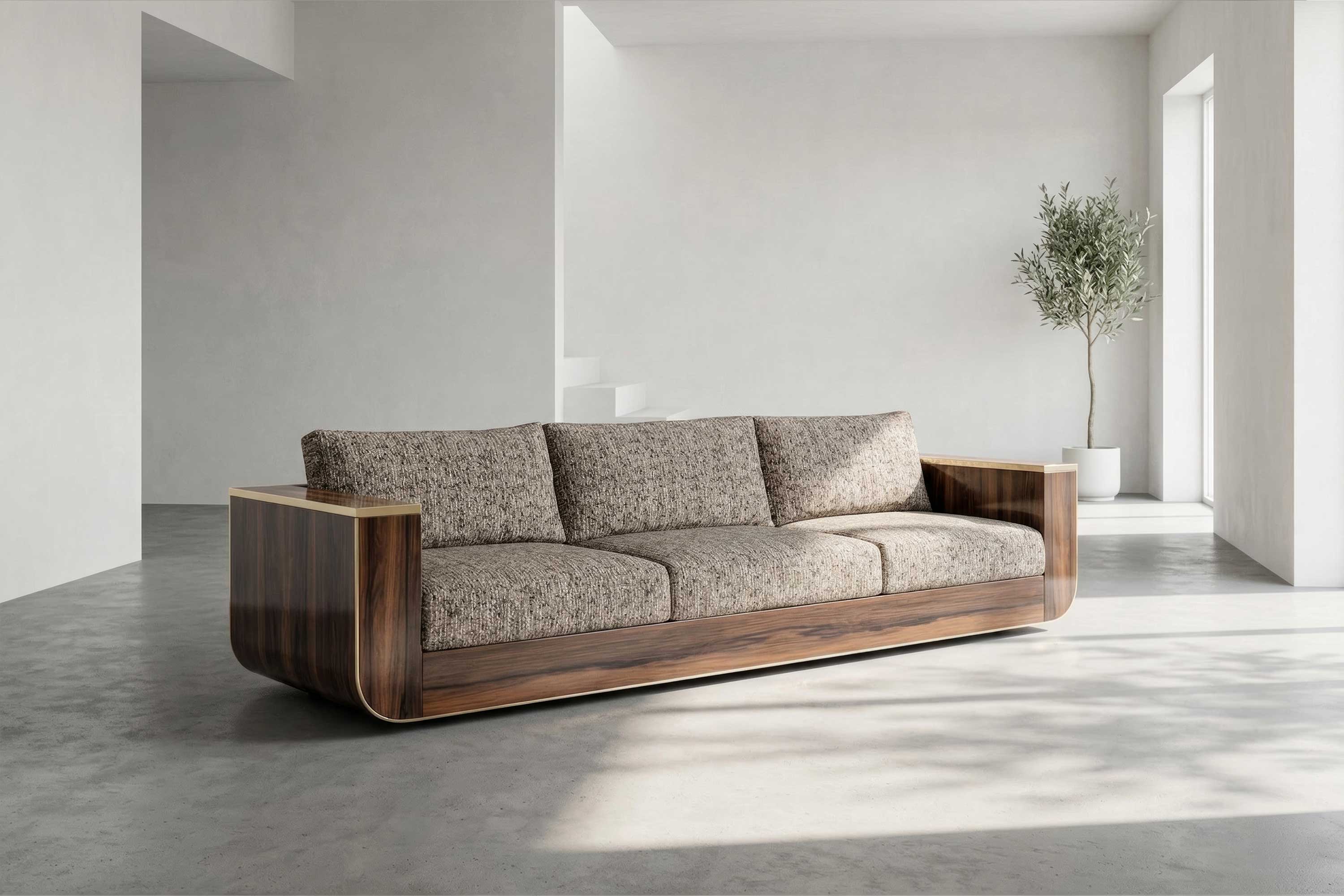 A modern sofa with a bespoke furniture wooden frame and three patterned cushions sits in a minimalist room with light gray walls, concrete floor, a potted plant, and natural light from large windows.