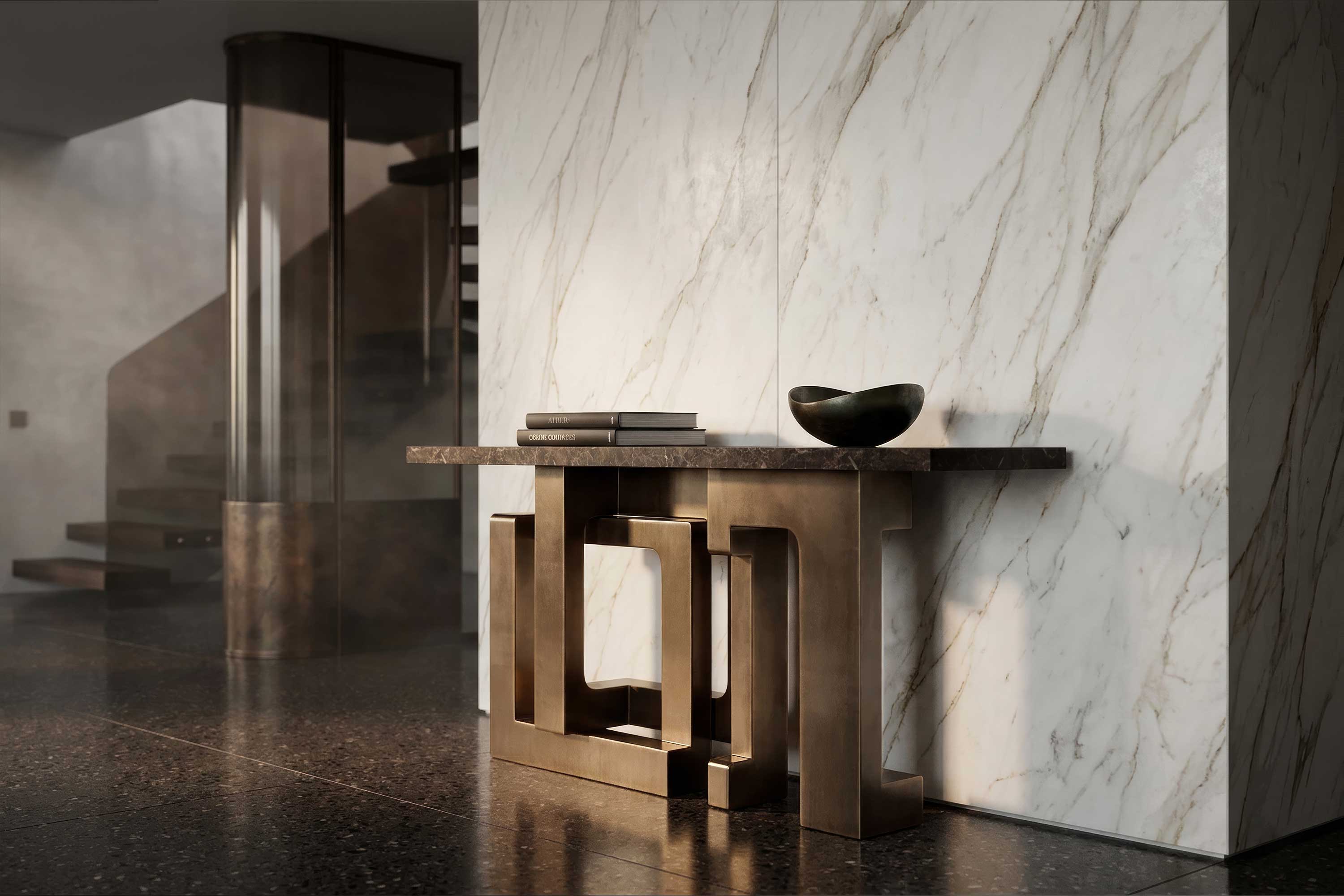 A modern entryway features a geometric gold console table against a marble wall, with two stacked books and a small black bowl on top. A staircase with glass railing is visible in the background.
