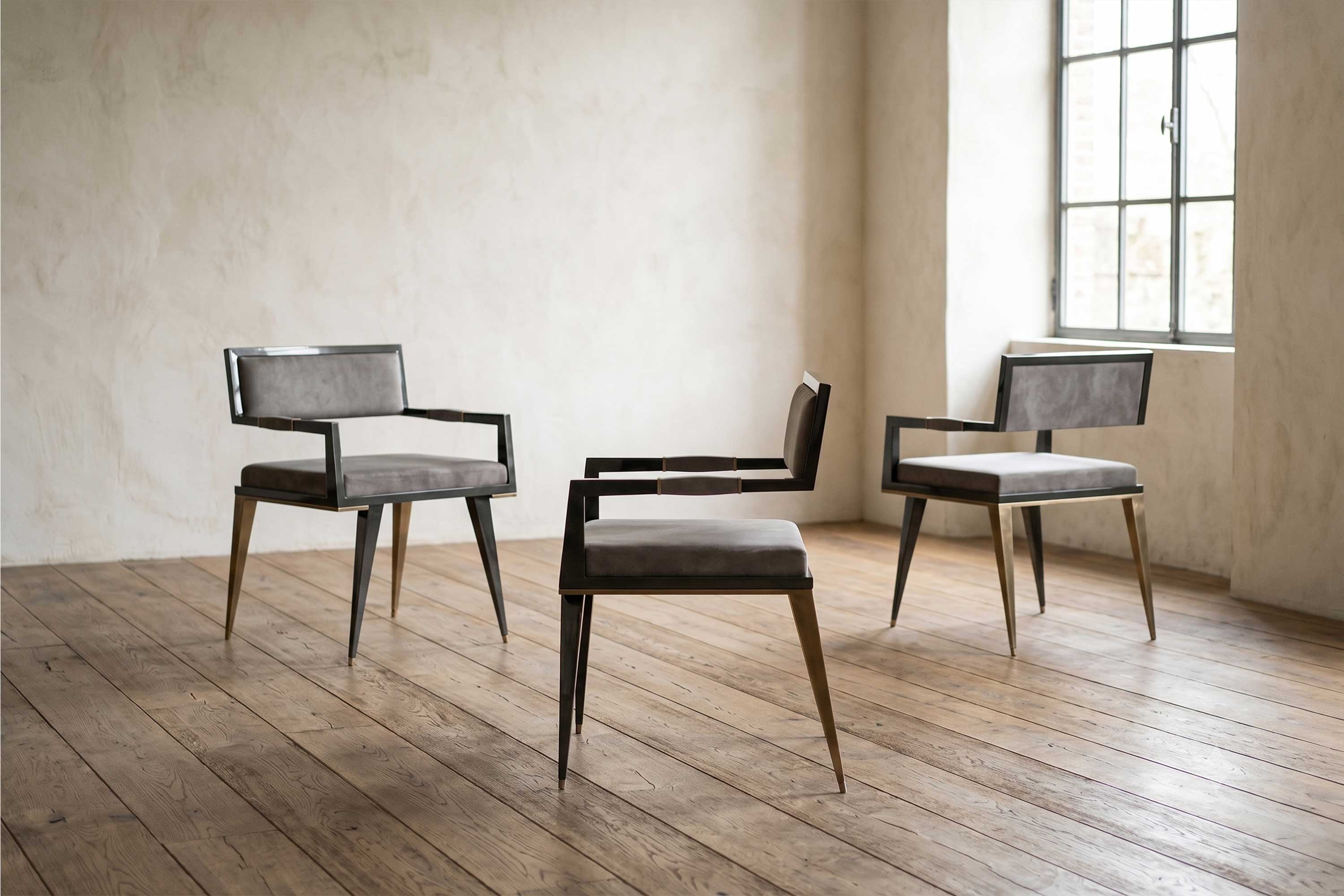 Three modern chairs with metal frames and gray cushions are arranged on a wooden floor in a minimalist room with light-colored walls and a large window. Natural light enters from the window on the right.