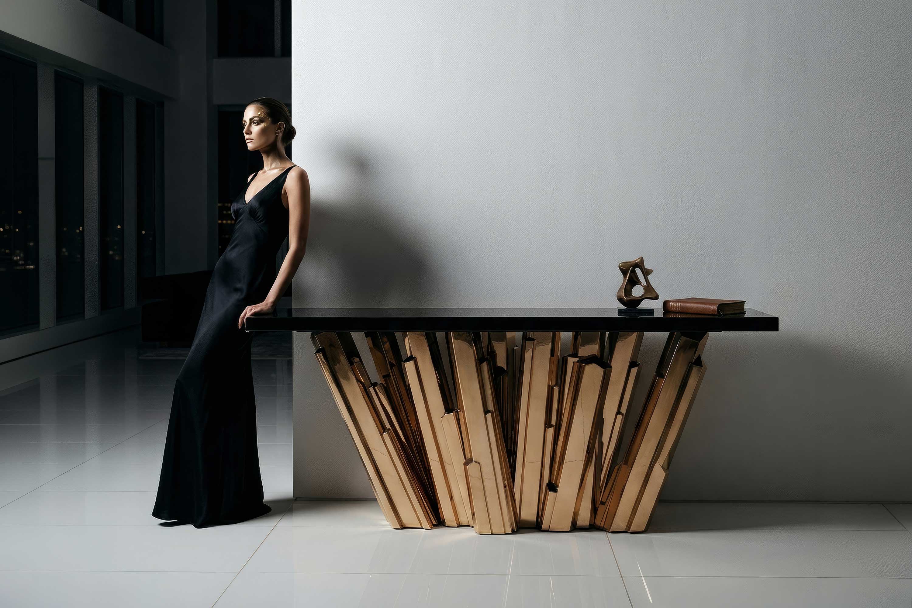 A woman in a black gown leans against a modern table with a sculptural wooden base. The table holds a small sculpture and a closed book. The setting is a minimalist, upscale room with large windows.