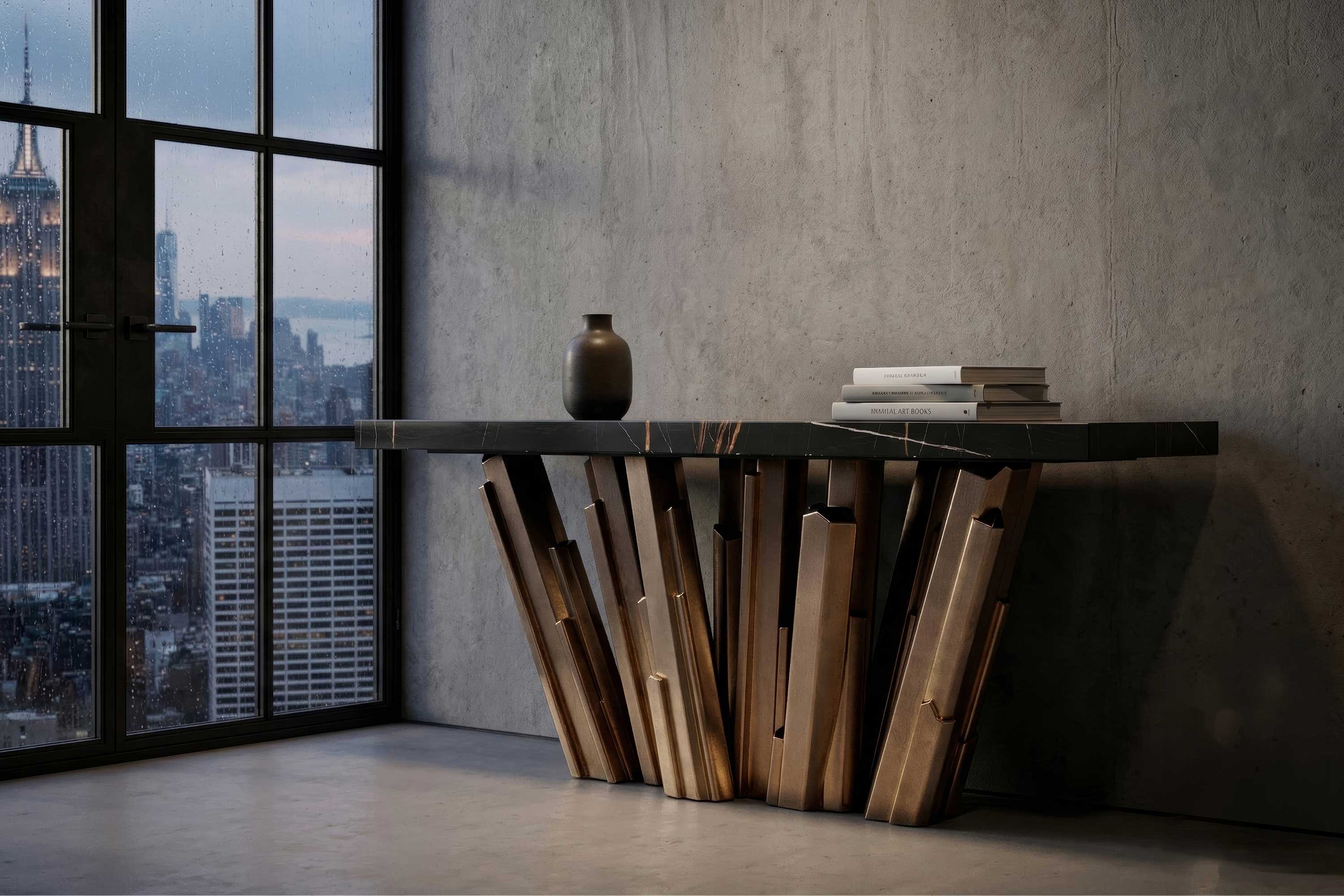 A modern console table with a geometric wooden base and black marble top stands against a gray concrete wall. A ceramic vase and stacked books sit on the table. City buildings are visible through a large window.
