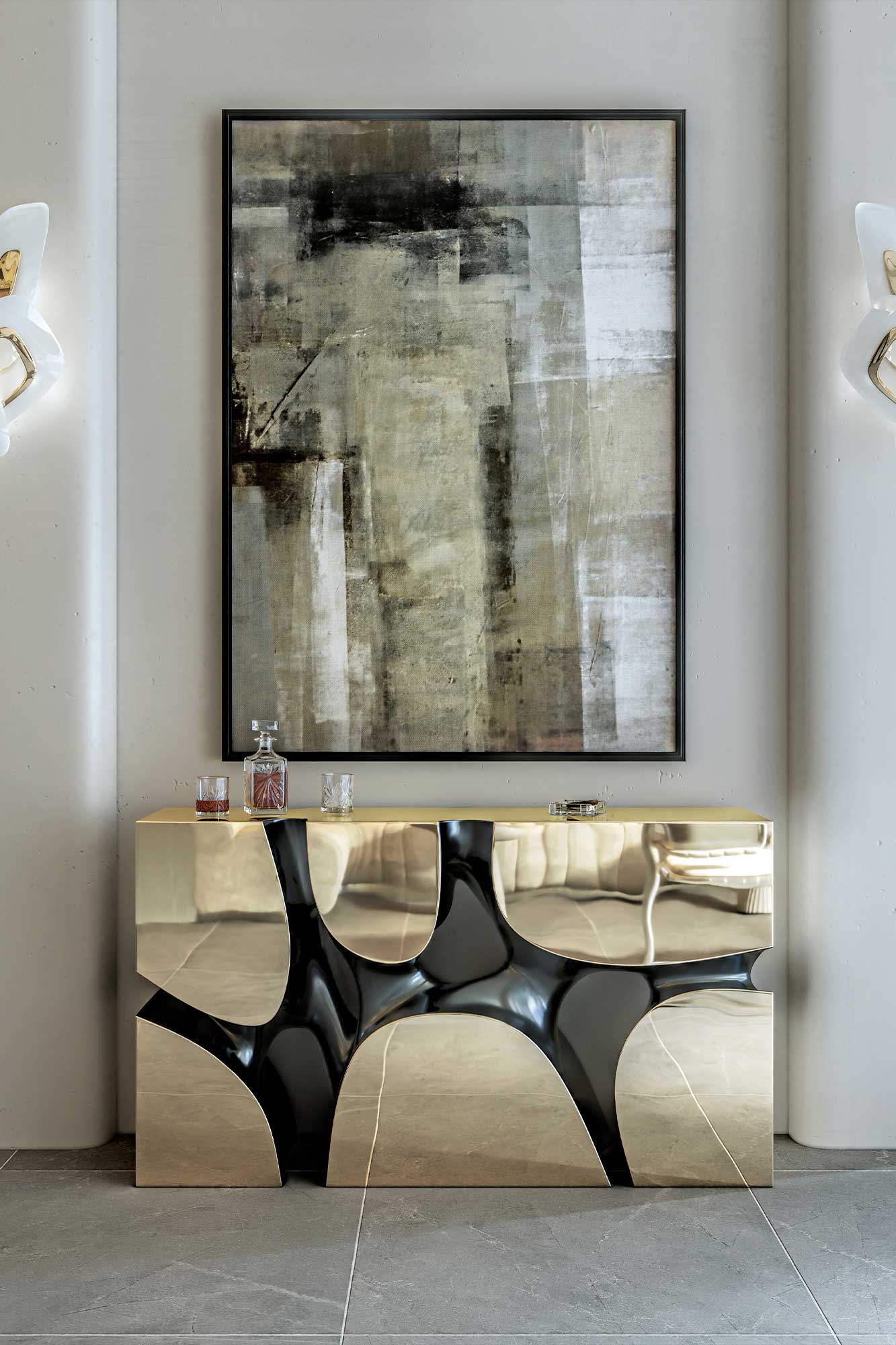 A gold and black geometric console table stands against a wall, topped with glassware. Above it hangs a large abstract painting in neutral tones. Sconces are mounted on both sides. The floor is made of stone tiles.