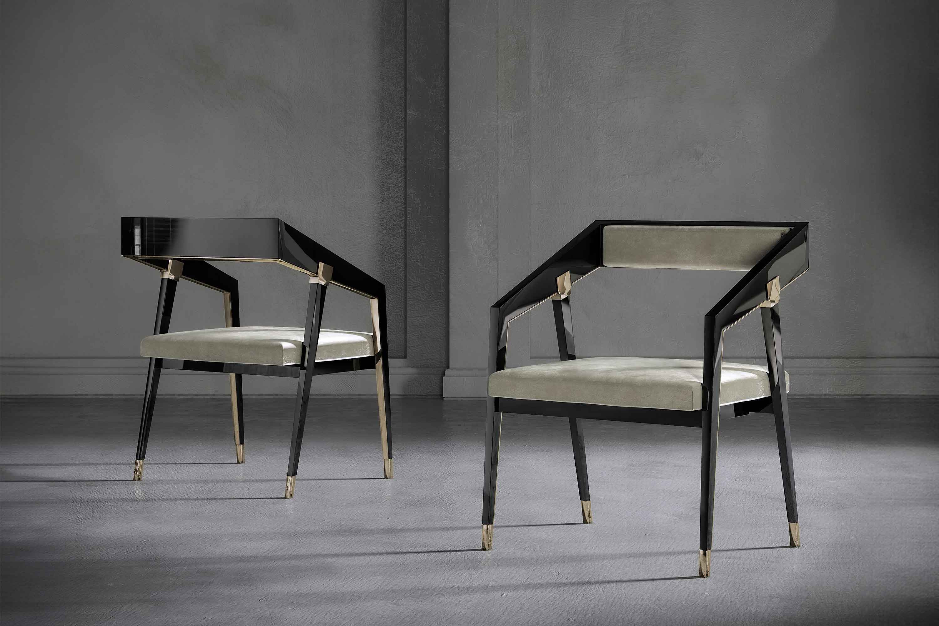 Two modern chairs with black angular frames, gold accents, and light gray upholstered seats and backs are positioned on a plain gray floor against a gray wall.
