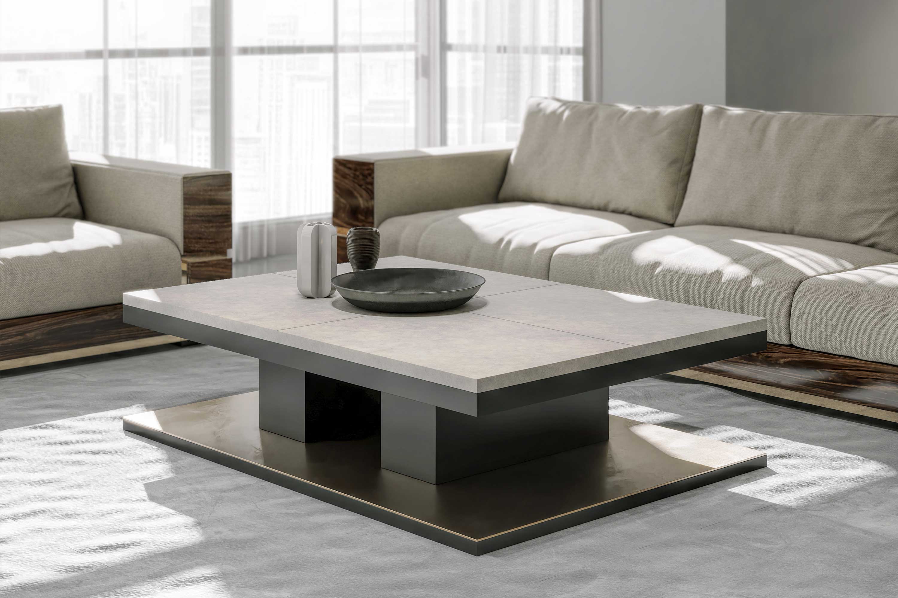 A modern living room with two beige sofas, a square coffee table with a thick stone top and dark base, and decorative vases and a bowl on the table. Large windows in the background let in natural light.