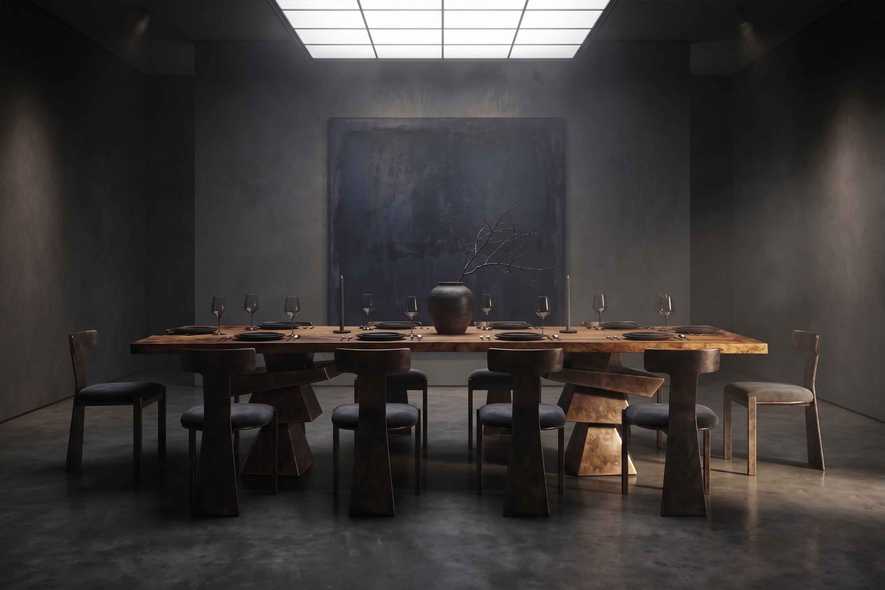 A large wooden dining table with eight chairs, set with plates, glasses, and cutlery. A dark vase with branches sits in the center. The room is dimly lit with a skylight and has dark walls and a minimalist style.