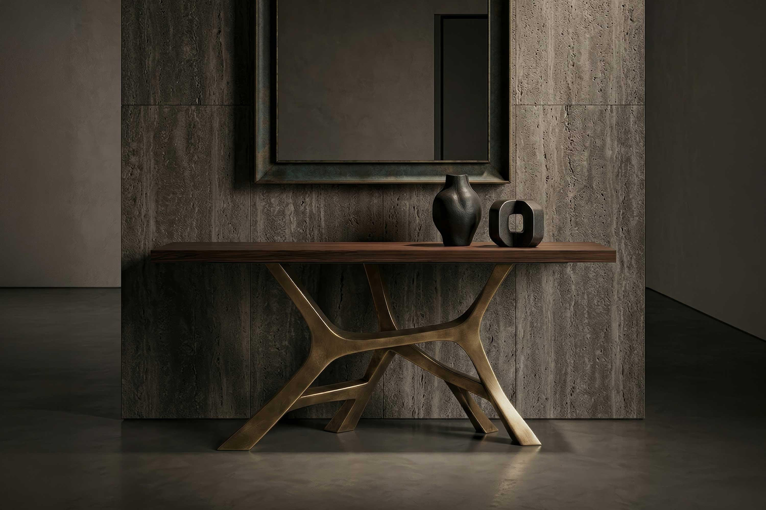 A wooden console table with a gold sculptural base stands against a gray stone wall. On the table are two black decorative vases. A large framed mirror hangs above, reflecting part of the muted room.