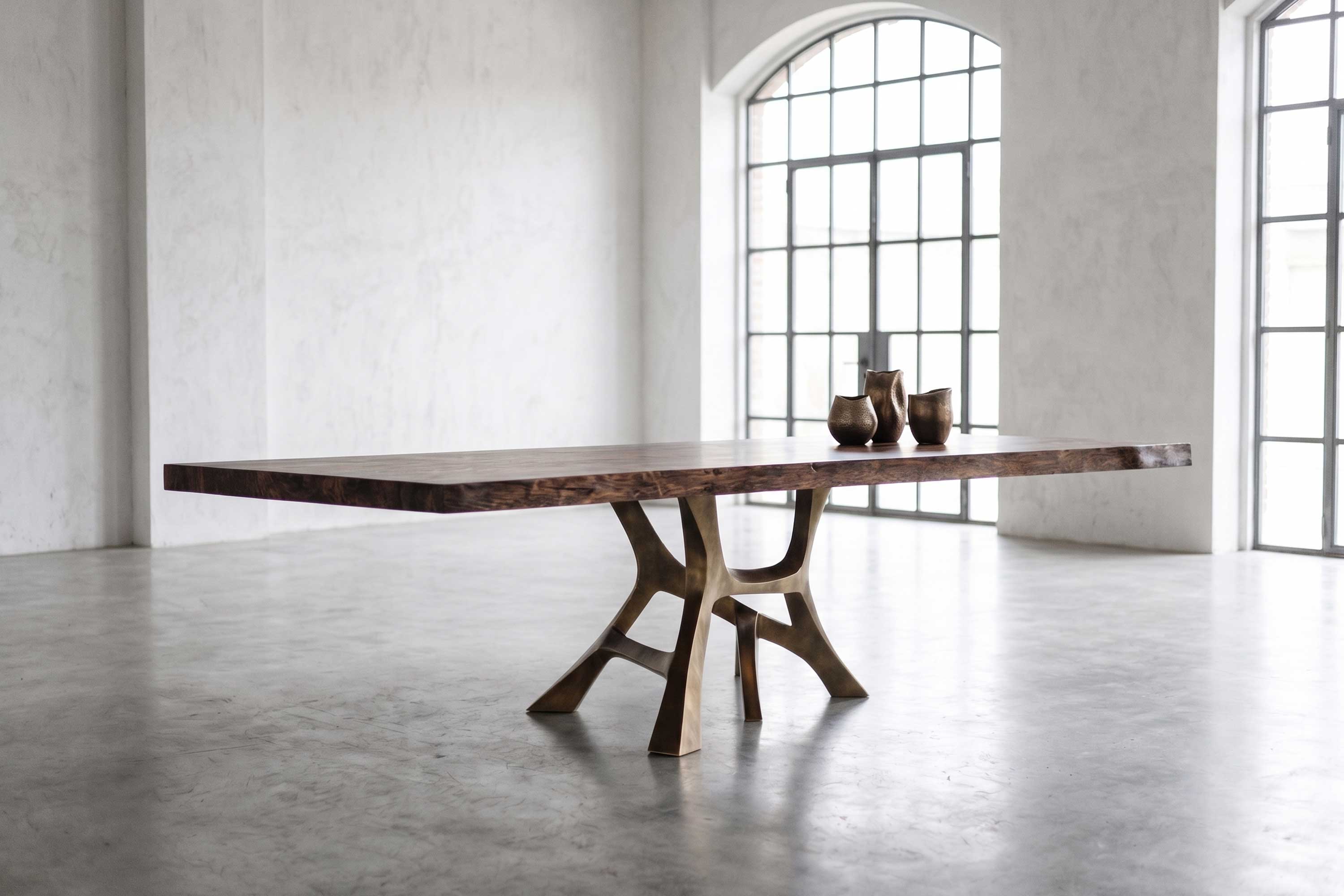 Vena Dining Table in Patina base and walnut tabletop in a minimal white interior with large windows on the background